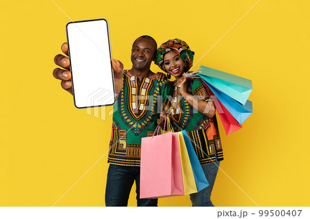 Beautiful black couple in traditional costumes customers showing phone, mockup 99500407