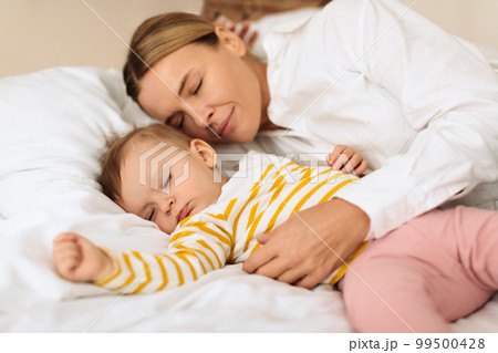Peaceful mother and cute little child girl lying on bed, sleeping together, mom embracing daughter during daytime sleep Peaceful mother and cute little child girl lying on bed, sleeping together, mom embracing daughter during daytime sleep 99500428