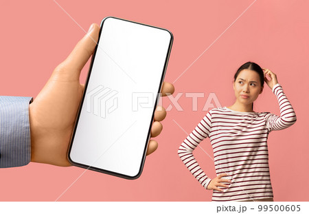 Doubtful Asian Woman Looking Aside At Blank Smartphone In Huge Male Hand Doubtful Asian Woman Looking Aside At Blank Smartphone In Huge Male Hand 99500605