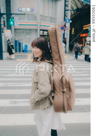 ギターを持って街を歩く女性の写真 99503061