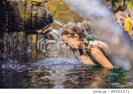 Woman in holy spring water temple in bali. The temple compound consists of a petirtaan or bathing structure, famous for its holy spring water 99503571