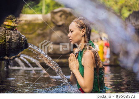 Woman in holy spring water temple in bali. The temple compound consists of a petirtaan or bathing structure, famous for its holy spring water 99503572
