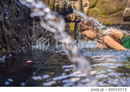 Woman in holy spring water temple in bali. The temple compound consists of a petirtaan or bathing structure, famous for its holy spring water 99503573