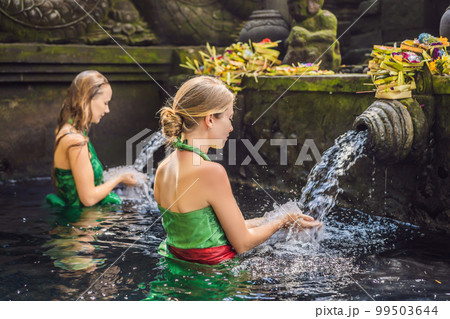 Two women in holy spring water temple in bali. The temple compound consists of a petirtaan or bathing structure, famous for its holy spring water 99503644