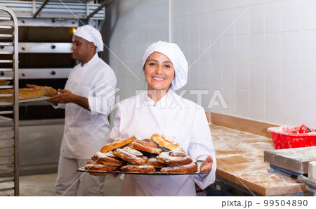 Cheerful woman baker with tray of sweet ensaimadas 99504890