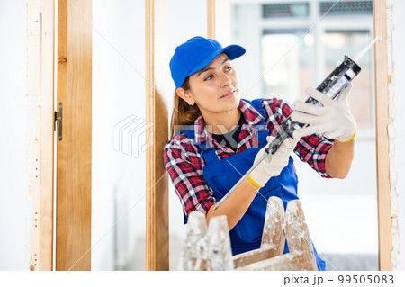 Woman builder using spray foam around doorway 99505083