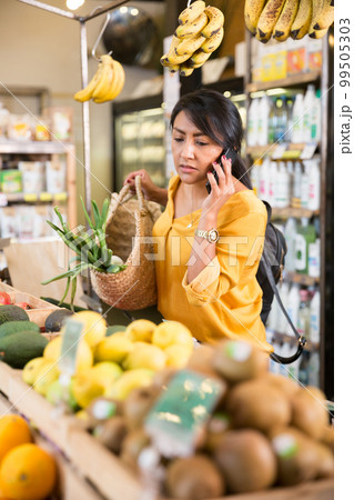 Woman talking on phone while buying vegetables and fruits in supermarket 99505303