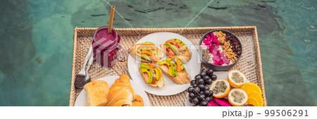 BANNER, LONG FORMAT Breakfast tray in swimming pool, floating breakfast in luxury hotel smoothies and fruit plate, smoothie bowl by the hotel pool. Exotic summer diet. Tropical beach lifestyle. Bali 99506291
