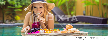 BANNER, LONG FORMAT Breakfast tray in swimming pool, floating breakfast in luxury hotel. Girl relaxing in the pool drinking smoothies and eating fruit plate, smoothie bowl by the hotel pool. Exotic 99506305