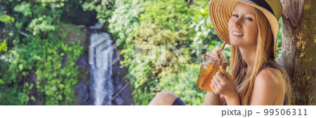 Closeup portrait image of a beautiful woman drinking ice tea with feeling happy in green nature and waterfall garden background BANNER, LONG FORMAT 99506311
