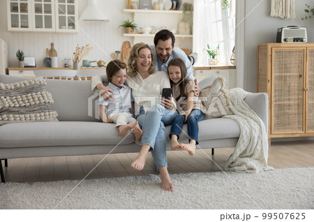 Cheerful mom, dad and two little kids using mobile phone Cheerful mom, dad and two little kids using mobile phone 99507625