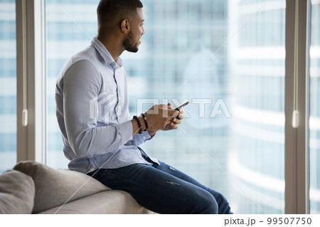 Dreamy handsome young African business man holding mobile phone Dreamy handsome young African business man holding mobile phone 99507750