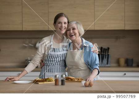 Joyful pretty older mom and adult daughter woman wearing aprons Joyful pretty older mom and adult daughter woman wearing aprons 99507769