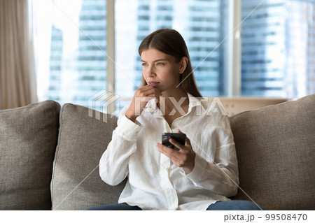 Pensive young millennial woman lost in thoughts holding cellphone 99508470