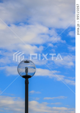 青い空と白い雲が街灯のガラスの中に写しこむ 99515097