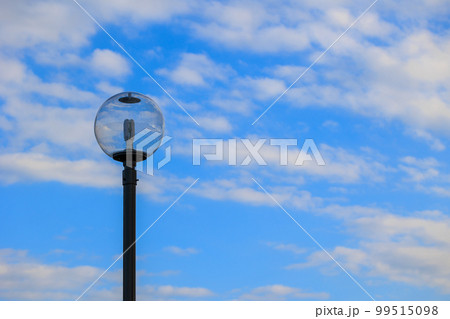 青い空と白い雲が街灯のガラスの中に写しこむ 99515098