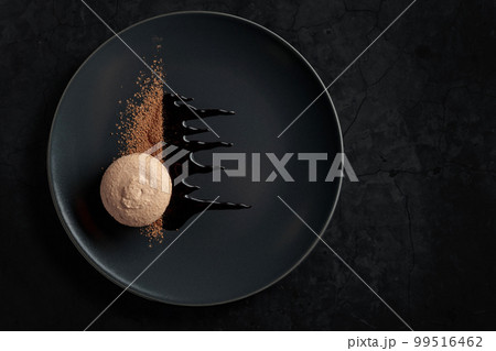 Macaroon on a black plate garnished with chocolate sauce and cocoa powder. Macaroon on a black plate garnished with chocolate sauce and cocoa powder. 99516462
