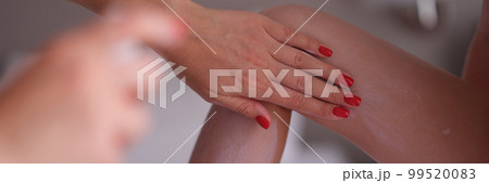 Mom applies sunscreen spray on daughter legs closeup 99520083