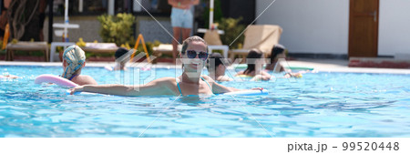 Young woman in sunglasses swims with aqua noodles in pool 99520448