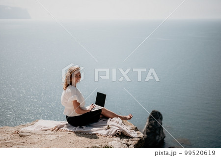 Woman sea laptop. Successful business woman working on laptop by the sea. Pretty lady typing on computer at summer day outdoors. Freelance, digital nomad, travel and holidays concept. Woman sea laptop. Successful business woman working on laptop by the sea. Pretty lady typing on computer at summer day outdoors. Freelance, digital nomad, travel and holidays concept. 99520619