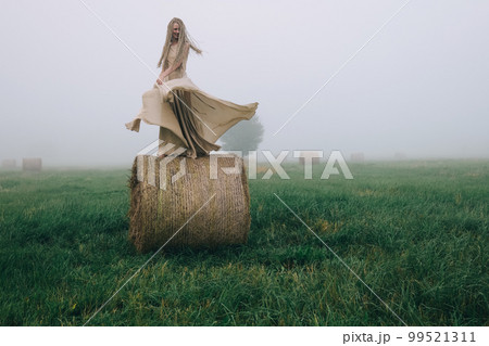 Young woman in beige dress dancing on haystacks at twilight time Young woman in beige dress dancing on haystacks at twilight time 99521311