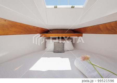 Bright luxury comfortable yacht inside with wood trim with white terry sheets, pillows, flower and sunbeams breaking through. Concept of luxury vacation on your own small yacht. Bright luxury comfortable yacht inside with wood trim with white terry sheets, pillows, flower and sunbeams breaking through. Concept of luxury vacation on your own small yacht. 99521596