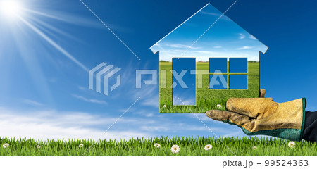 Gloved Hand Holding a Small Model House on a Rural Scene 99524363