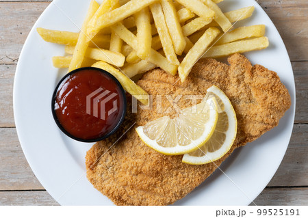 Wiener schnitzel with fried potatoes on wooedn table 99525191