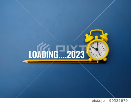 Pencil and alarm clock with the word LOADING 2023 on blue background. 99525670