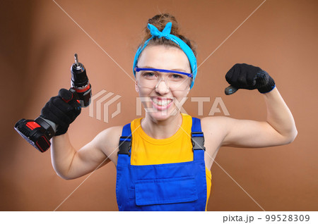 Smiling young caucasian woman in goggles with a screwdriver in her hands and in uniform stands in the studio Smiling young caucasian woman in goggles with a screwdriver in her hands and in uniform stands in the studio 99528309