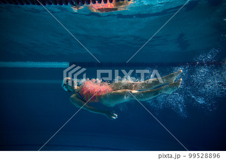 Swimming on back. Professional female swimmer training in swimming pool indoor. Cap and goggles. Underwater view. Concept of sport, endurance, competition 99528896