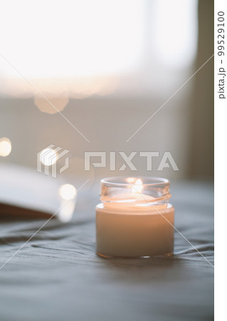 Cozy still life composition with a scented burning candle in glass jar in bed close up. Good morning. Cozy home 99529100