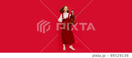 Portrait of little girl, talanted musician wearing huge mother's sundress playing violin, having fun isolated over magenta background. Education, music, classic art, new vision, fun concept 99529136