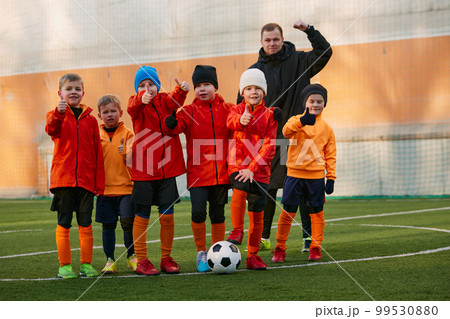 Group of boys, children, football players in uniform standing in a line on sports field grass outdoor, posing with coach. Concept of sport, childhood, active lifestyle Group of boys, children, football players in uniform standing in a line on sports field grass outdoor, posing with coach. Concept of sport, childhood, active lifestyle 99530880