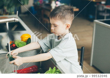 Six-year-old boy washing vegetables in the kitchen sink. Side view. Six-year-old boy washing vegetables in the kitchen sink. Side view. 99532046