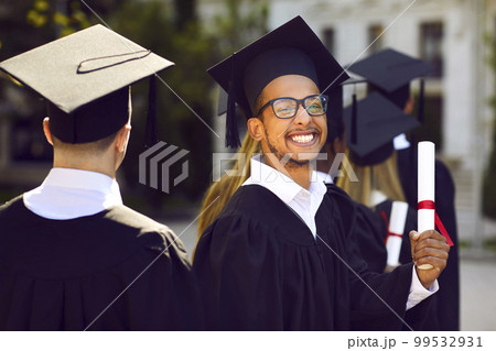 Excited college graduate man in black mortar board cap holding diploma Excited college graduate man in black mortar board cap holding diploma 99532931
