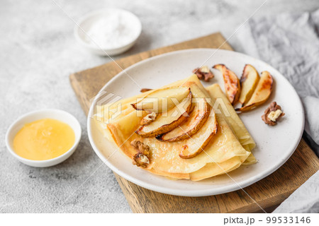 Delicious fresh baked pancakes with honey and fruits on a textured concrete background Delicious fresh baked pancakes with honey and fruits on a textured concrete background 99533146