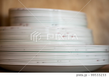 Narrow depth of field picture of an open kitchen cabinet stacked ceramic plates and bowls. 99533233