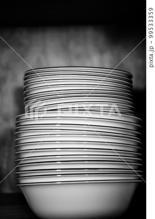 Narrow depth of field picture of an open kitchen cabinet stacked ceramic plates and bowls. 99533359