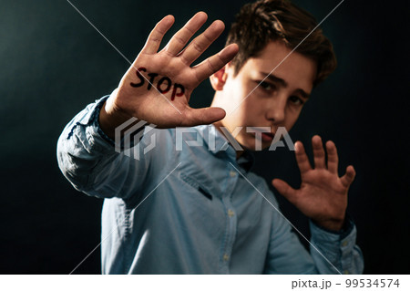 The concept of domestic violence. Sad teenager puts his hands in front of him defending himself from the threat of attack. Black background. Text STOP The concept of domestic violence. Sad teenager puts his hands in front of him defending himself from the threat of attack. Black background. Text STOP 99534574