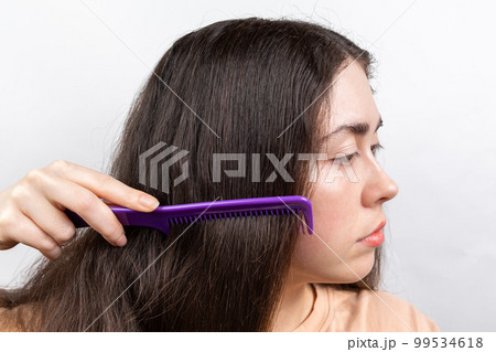 Dandruff and hair problems. A woman combs her long dark hair. Side view. White background 99534618