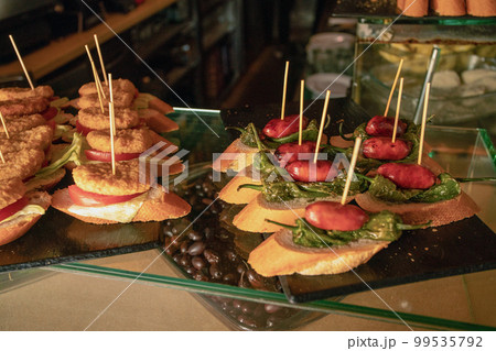 tapas (pintxos, sandwich) with small sausage and salted peppers, bread and tapas with a cutlet (chicken?) and in a cafe in Barcelona tapas (pintxos, sandwich) with small sausage and salted peppers, bread and tapas with a cutlet (chicken?) and in a cafe in Barcelona 99535792