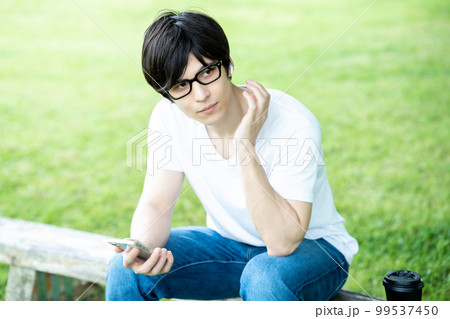 新緑の公園でスマホ音楽を聴く眼鏡の男性 99537450