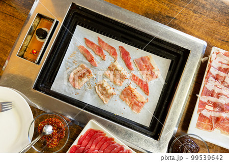 Thin slices of beef laid out on korean barbeque grill on table with barbeque seasoning on the side 99539642