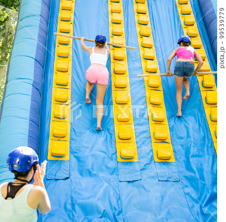 Women using sticks to reach top of slide in adventure park Women using sticks to reach top of slide in adventure park 99539779