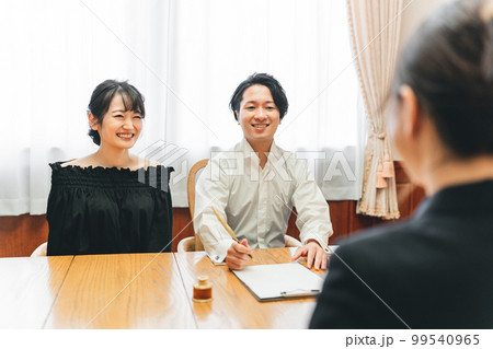コンシェルジュ・ホテリエ・ウェディングプランナーと打ち合わせして契約書にサインする男女（結婚相談所） 99540965
