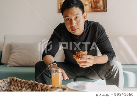 Man having bread and juice as breakfast on the sofa living room. Man having bread and juice as breakfast on the sofa living room. 99541660