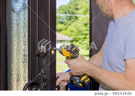 During construction of new home carpenter worker installs new lock on front door using screwdriver 99543936