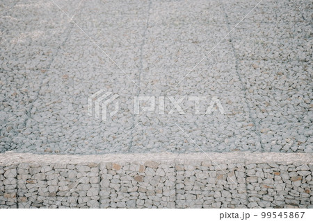 Granite stones behind a metal grate for strengthening the slope. Stones behind the wire. grey texture. construction. 99545867