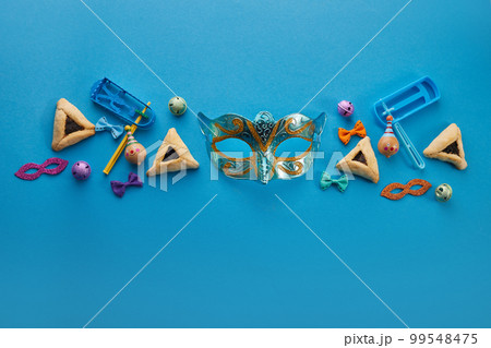 Purim celebration concept. Jewish carnival background. hamantaschen or hamans ears cookies, carnival mask and noisemaker Purim celebration concept. Jewish carnival background. hamantaschen or hamans ears cookies, carnival mask and noisemaker 99548475